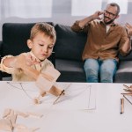 Zoontje spelen met houten vliegtuig model terwijl vader praten door smartphone achter