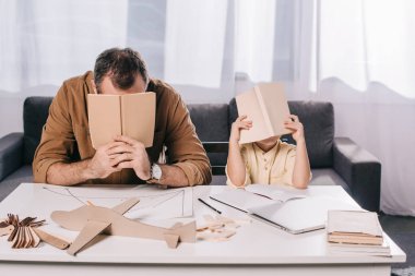 Baba ve oğul birlikte evde modelleme ise yüzler kitap arkasında saklanıyor