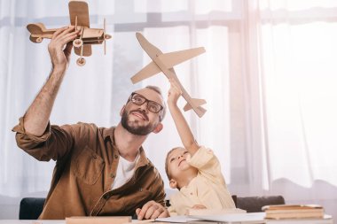 happy father and little son playing with wooden planes models at home clipart