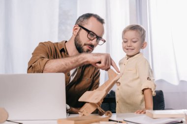 ahşap uçak modeli evde tutan babasına bakarak gülümseyen küçük oğlu