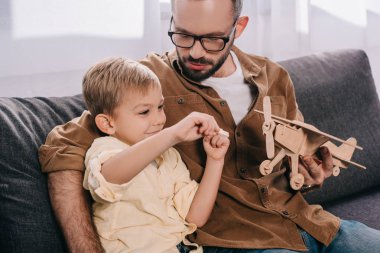 Baba ve kanepede oturan ve ahşap uçak modeli ile oynarken küçük oğul   