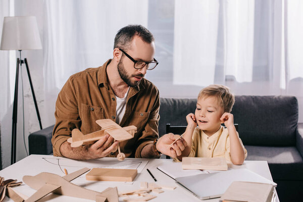 father in eyeglasses and smiling son modeling plane together at home 