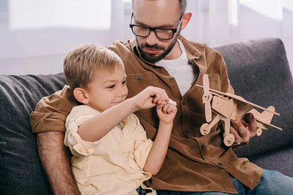 Father Little Son Sitting Couch Playing Wooden Plane Model — Free Stock Photo