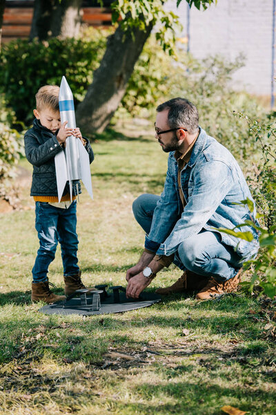father and son playing with model rocket together at sunny day  