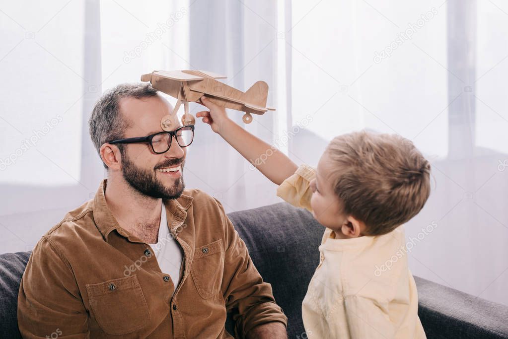 happy father and son playing with wooden toy plane at home