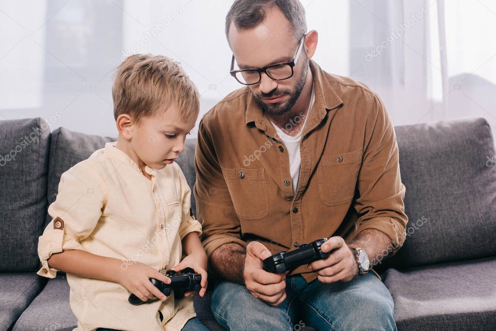 father and cute little son playing together with joysticks at home