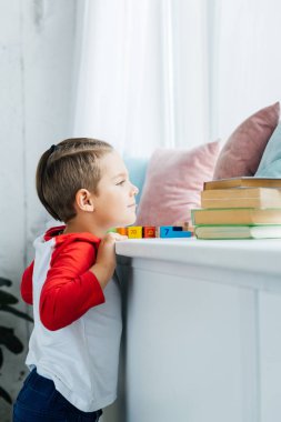 side view of child standing at surface with books and colorful blocks at home clipart