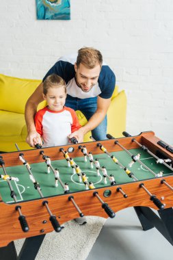 Baba ve oğul birlikte evde masa futbolu oynayan gülümseyen