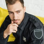 Close-up shot of thoughtful young policeman sitting on yellow couch