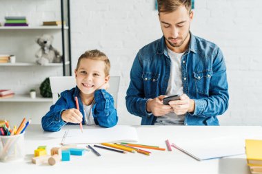 yakışıklı genç baba oğul evde çizim sırasında Smartphone kullanarak