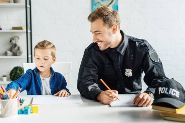 Polis üniforması ve küçük oğlu evde çizim birlikte mutlu genç baba