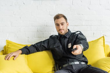 kanepede oturan ve tv uzaktan kumanda ile yakışıklı genç polis memuru