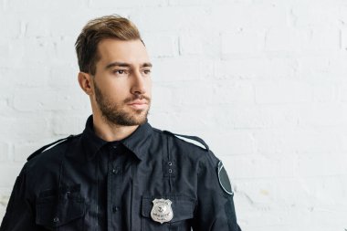 düşünceli genç polis memuru önünde beyaz tuğla duvar portresi