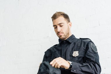 Beyaz tuğla duvarın önünde, ayakta çekici genç polis memuru