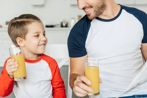 父亲和快乐的儿子的部分视图在早餐在厨房在家里的玻璃杯果汁 — 图库照片