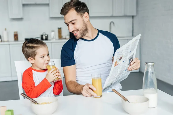 Pai Com Jornal Olhando Para Filho Beber Suco Durante Café — Fotografia de Stock