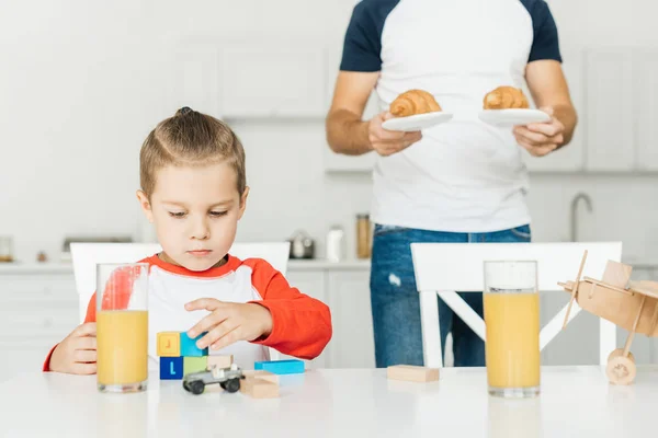 Cropped Shot Father Serving Croissants Breakfast Son While Playing Toys — Free Stock Photo
