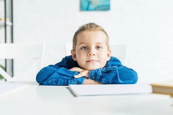 Adorável Criança Sentada Mesa Com Caderno Branco Olhando Para Câmera — Fotografia de Stock Grátis