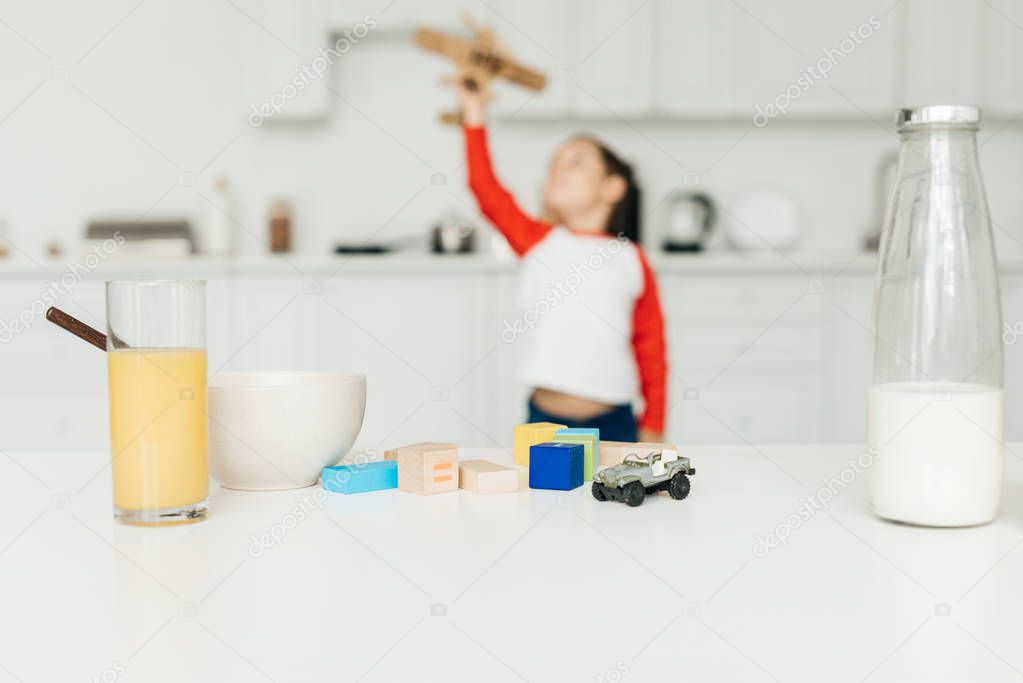 selective focus of little boy playing with toy wooden plane in kitchen at home