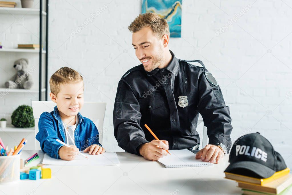 smiling young father in police uniform and son drawing together at home