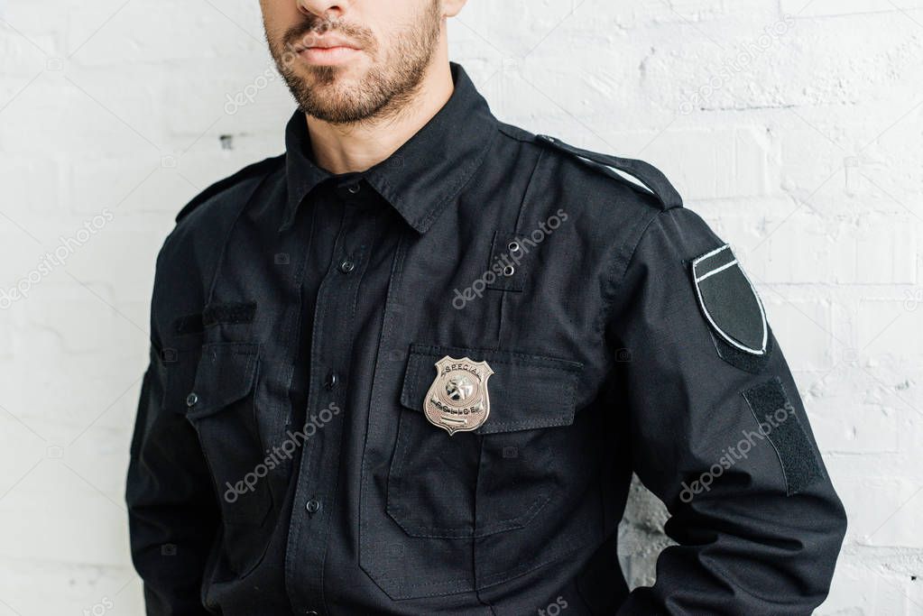 cropped shot of young policeman in front of white brick wall