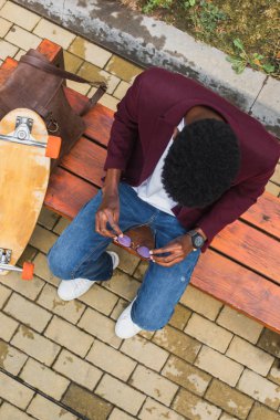 overhead view of young man with eyeglasses and skateboard sitting on bench clipart
