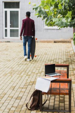 Dikiz kaykay ile laptop ve defter ön plan üzerinde bankta ile sokakta yürüyen adam