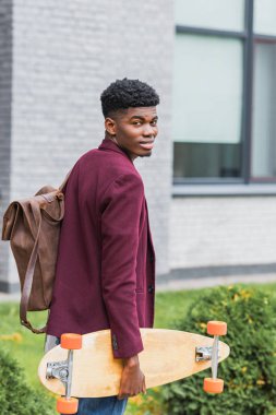 sırt çantası ve street tarafından yürüyüş ve kameraya bakarak kaykay ile gülümseyen genç öğrenci