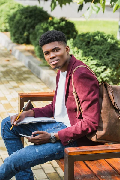 Joven Estudiante Guapo Usando Teléfono Inteligente Mientras Está Sentado Banco — Foto de Stock