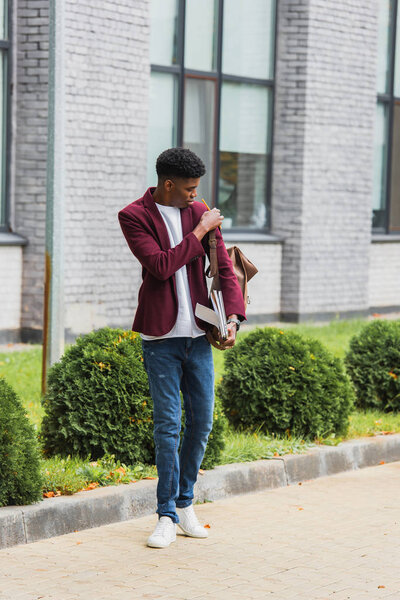 stylish young student with backpack and notebooks standing on street