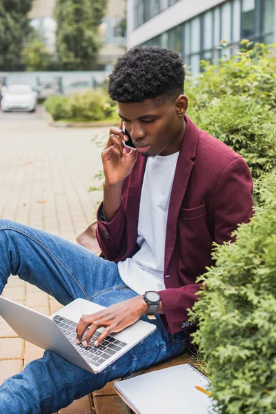 Young Freelancer Using Laptop Writing Notebook While Sitting Curb Street — Free Stock Photo