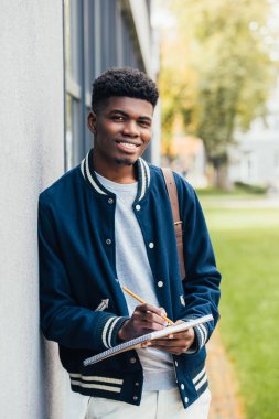 gülümseyen genç Afro-Amerikan öğrenci ders kitabı yazma 