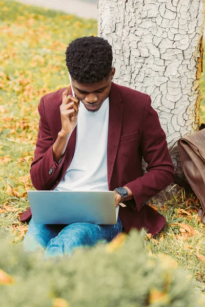 Африканский Американский Телеработник Использующий Ноутбук Разговаривающий Смартфоне Парке — Бесплатное стоковое фото