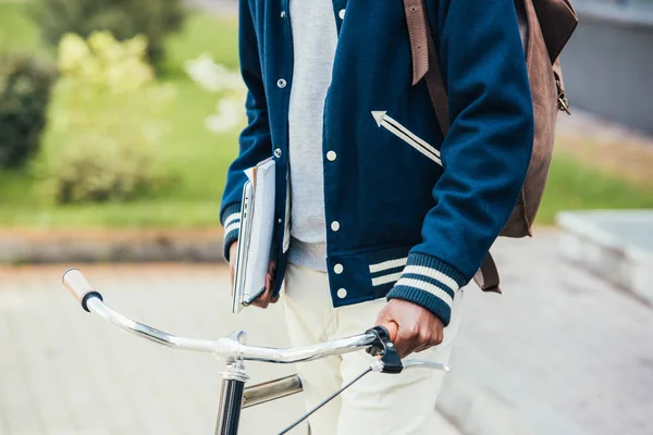 cropped view of male student with papers laptop and bicycle on street