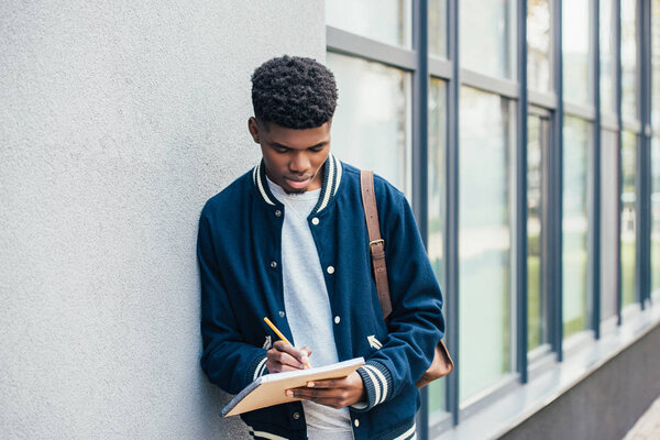 Концентрированный молодой африканский студент-американец пишет в учебнике
 