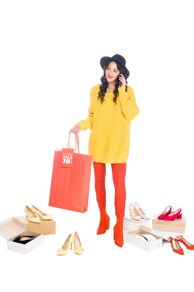 fashionable girl talking on smartphone and holding shopping bag with sale tag isolated on white with footwear boxes