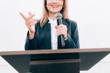 cropped image of smiling speaker gesturing and talking at podium tribune during seminar in conference hall clipart