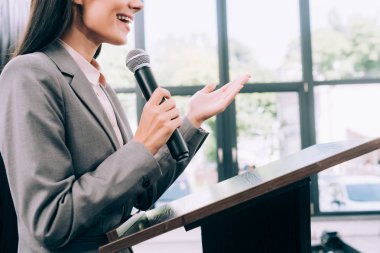 cropped image of smiling lecturer talking into microphone and gesturing at podium tribune during seminar in conference hall clipart