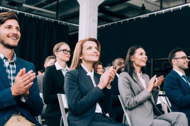 smiling multiethnic businesspeople applauding during business seminar in conference hall clipart