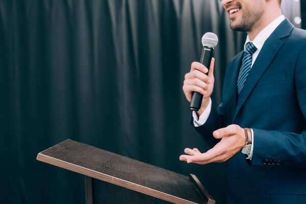 cropped image of speaker gesturing and talking into microphone at podium tribune during seminar in conference hall