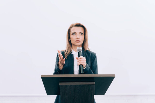 красивый оратор жестом и говорить в микрофон на трибуне подиума во время семинара в конференц-зале
