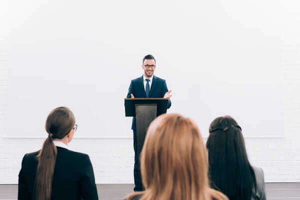 улыбающийся красивый преподаватель, выступающий перед аудиторией во время семинара в конференц-зале
