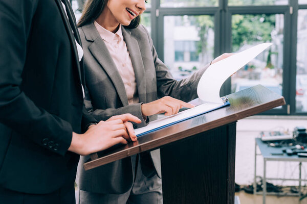 cropped image of assistant showing documents to speaker during seminar in conference hall
