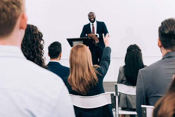 Африканский американский преподаватель беседует с аудиторией во время семинара в конференц-зале, участник поднимает руку
