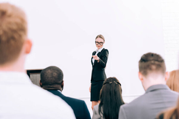 привлекательный преподаватель, указывающий на мультикультурную аудиторию во время семинара в конференц-зале
