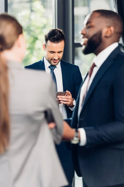 Foco Seletivo Empresário Usando Smartphone Enquanto Colegas Multiétnicos Conversando Escritório — Fotografia de Stock