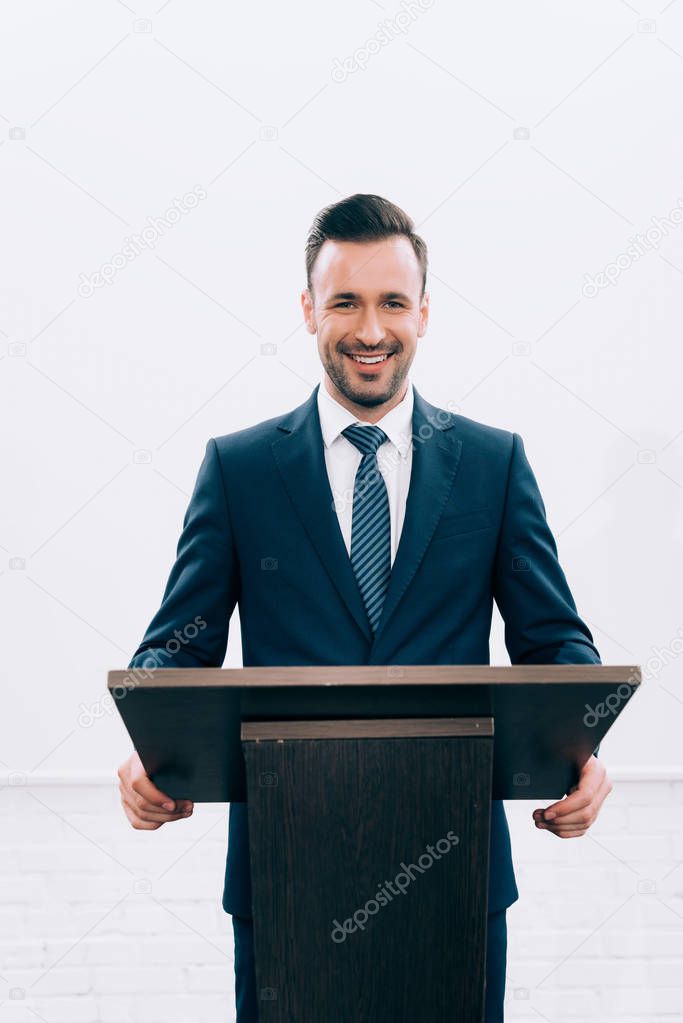 smiling lecturer standing at podium tribune during seminar in conference hall