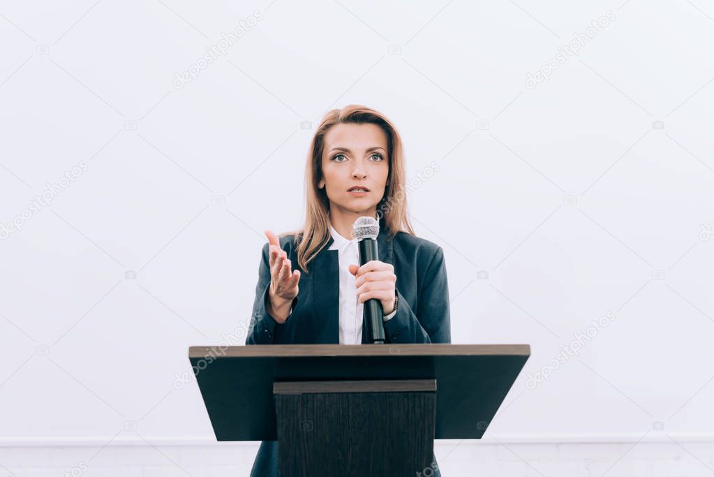 beautiful speaker gesturing and talking into microphone at podium tribune during seminar in conference hall