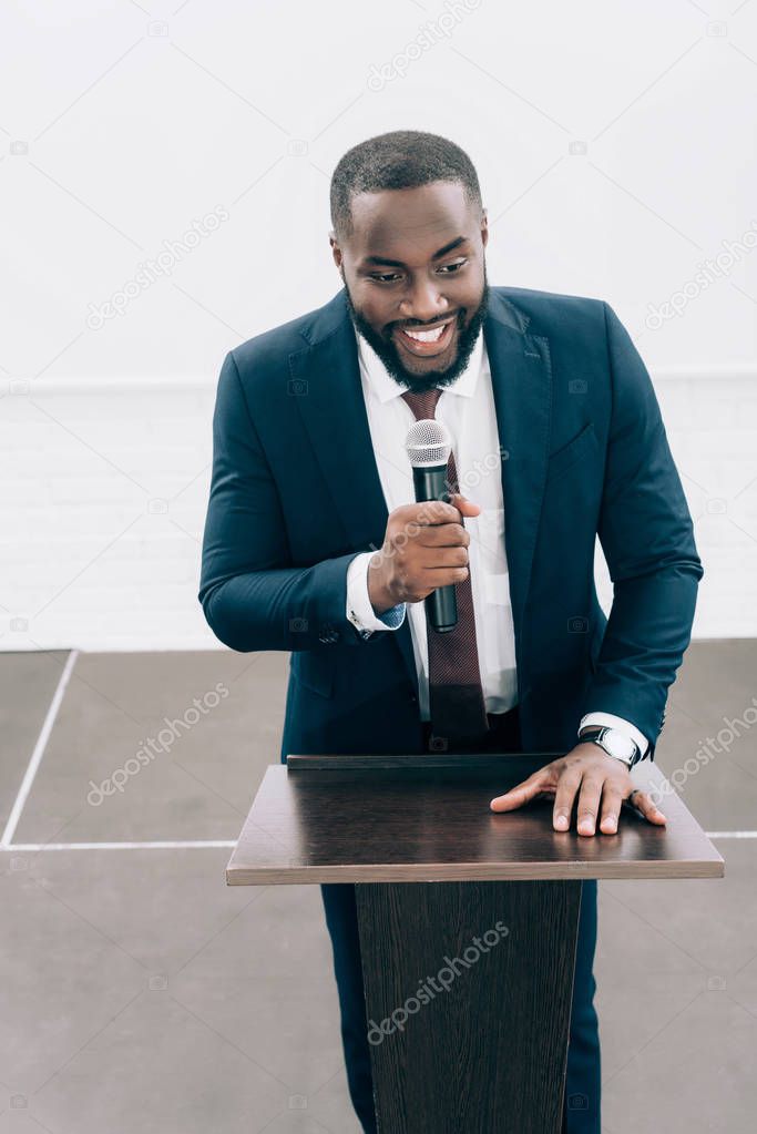 high angle view of smiling african american speaker talking into microphone during seminar in conference hall