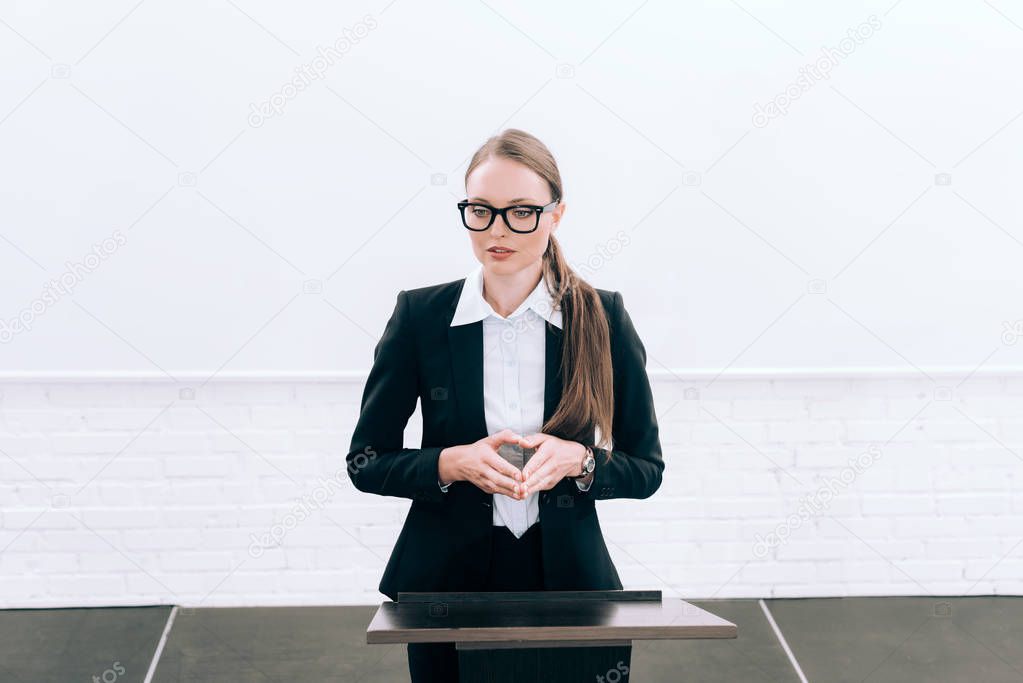 attractive lecturer in glasses standing at podium tribune during seminar in conference hall